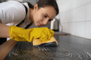 Person wearing yellow gloves cleaning a countertop with a sponge and soap suds in a kitchen, showcasing detailed cleaning for a spotless space.